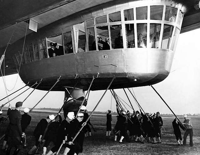 A closer look at the Hindenburg's gondola as sailors from Lakehurst Naval Air Station use guy poles to help the airship to its mooring. This was the Hindenburg's first US landing on May 9, 1936. Dr. Hugo Eckener can be seen at the far right in the gondola. Date Taken on 9 May 1936 Source eBay front back Oakland Tribune 10 May 1936, page 52 Author Associated Press/Oakland Tribune